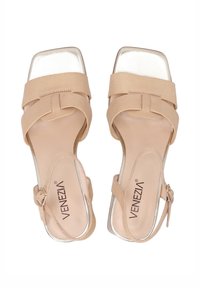 Beige højhalsede sandaler med firkantet tå, der har en justerbar ankelrem og metalliske sølvdetaljer på hælen og sålen.