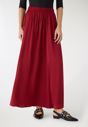 Donna che indossa una lunga gonna rossa con vita elastica, abbinata a scarpe slingback nere con punta appuntita, fibbia e dettagli a occhiello.