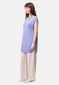 Helllila ärmellose Strick-Tunika mit strukturiertem Design, kombiniert mit weit geschnittenen, gestreiften Hosen in Pastellfarben und flachen beigen Schuhen.