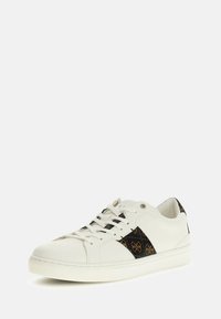 Zapatilla blanca con parte superior de cuero suave, paneles laterales con patrones en tonos oscuros, punta redonda y suela plana de goma blanca.