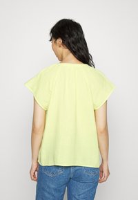Top curto amarelo claro com um corte solto, tecido texturado e decote redondo, combinado com jeans azuis.