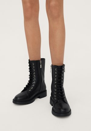Black leather combat boots with round toe, front lacing, silver eyelets, side zipper, and textured rubber sole. Minimalist design and sturdy construction.
