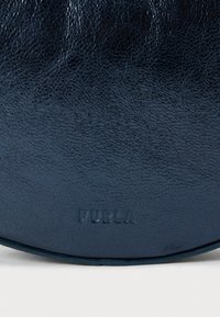 Granatowa torebka ze tłoczonej skóry o gładkim wykończeniu, z wytłoczonym logo "Furla" na dolnej krawędzi, okrągły kształt, minimalistyczny design.