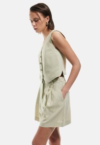 Completo in due pezzi in lino composto da un gilet verde chiaro con bottoni e un design di pantaloni corti plissettati, caratterizzato da tasche laterali e una vestibilità rilassata.