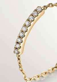 Pulsera de oro con una barra curva central que presenta nueve diamantes redondos engastados en garras, unida a una banda de eslabones.