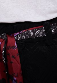 Tissu noir avec un motif texturé, doté d'une ceinture multicolore à imprimé cachemire et d'un détail de lien en satin rouge contrastant.