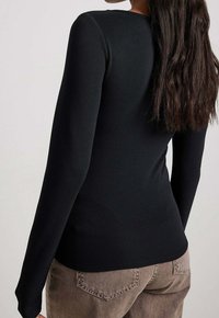 Haut noir à manches longues avec une texture finement côtelée, doté d'un col rond. Le vêtement est ajusté, associé à un pantalon en velours côtelé marron clair.
