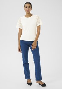Cream top with lace short sleeves, paired with blue straight-leg jeans. The top features a round neck and a smooth texture; jeans have a classic design.