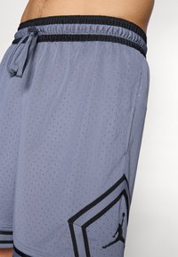 Pantalones cortos deportivos grises con textura perforada, cinturilla elástica negra y un gran logo de jumpman negro en el lado inferior izquierdo.