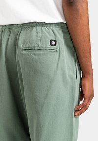Groene katoenen broek met een gestructureerde afwerking, voorzien van een zwart logo-label op de achterzak en een zijzakdetail.