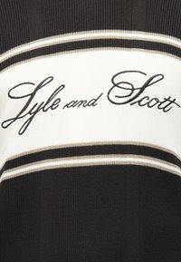 Πλεκτό ύφασμα σε ασπρόμαυρο με οριζόντιες ρίγες και κεντημένο με γραφικό χαρακτήρα το "Lyle and Scott" στο κέντρο.