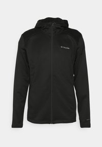 Svart Columbia-jacka med hel dragkedja och huva, långa ärmar och logotyp på bröstet och ärmen, framför en neutral bakgrund.