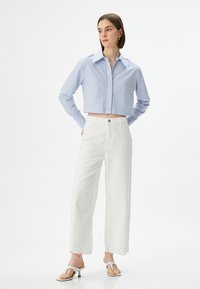 Camicia a righe blu e bianche, corta, con colletto a punta, abbinata a pantaloni bianchi a gamba larga con orli ricamati e sandali flat.