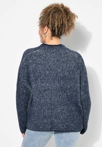 Dunkelblauer gerippter Pullover mit hohem Kragen, oversized Schnitt und strukturiertem Material, kombiniert mit hellblauen Jeans.