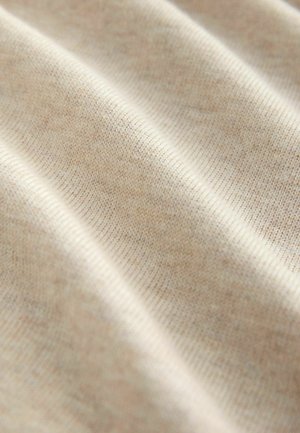 Helle beige Stoff mit feiner Strickstruktur, die subtile Farbvariationen und enge Stiche zeigt, die sanfte Wellen und Falten bilden.