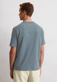 T-shirt rayé en bleu et crème, présentant des manches courtes et un col rond. Le tissu semble doux avec une coupe décontractée.