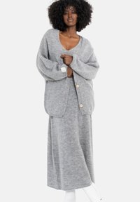 Szary dzianinowy kardigan z dużymi rękawami i drewnianymi guzikami, zestawiony z dopasowaną długą spódnicą. Miękka faktura, swobodny fason.