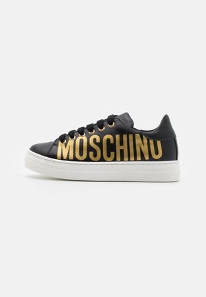 Zwarte leren sneaker met witte zool, zwarte veters en groot gouden MOSCHINO-logo aan de zijkant.
