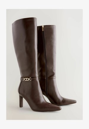 Brūni ceļgala augstuma zābaki ar papēdi, izgatavoti no gludas ādas, ar sānu rāvējslēdzēju, norakstītu purngalu un zelta toņu sprādzi ap potīti.