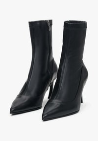 Černé kožené kotníkové boty s špičatými špičkami a elegantním siluetou. Mají boční zip, vysoké jehlové podpatky a hladký povrch.