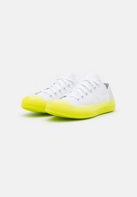 Baskets en toile blanche avec semelles et bouts en caoutchouc jaune vif. Comprend six œillets pour les lacets et un design bas.