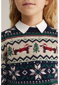 Stickad tröja med marinblå botten samt creme, grön och röd färg. Innehåller taxar, träd och snöflingor i ett mönster. Vit krage syns.