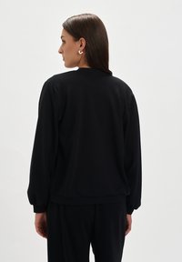Czarna bluza z długim rękawem i okrągłym dekoltem, z ribbowanymi mankietami, wykonana z miękkiego materiału. Prosty design bez widocznych wzorów czy logo.