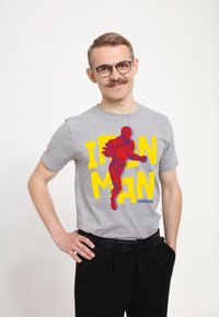 Szara bawełniana koszulka z grafiką Iron Mana w czerwonych i żółtych kolorach oraz napisem "IRON MAN" i "ENDGAME" w wyrazistych kolorach. Czarne spodnie.