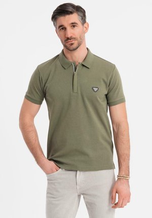 Olivgrünes Poloshirt aus Baumwolle mit kurzem Kragen, zwei Druckknöpfen und einem dreieckigen Markenlogo auf der Brust.