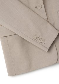 Manche de blazer beige avec quatre boutons recouverts de tissu et une partie du corps du blazer montrant un bouton unique et une poche.