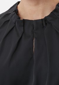 Sort bluse med plisseret halsudskæring og en lille åbning foran, lavet af blødt, glat stof med en subtil glans.