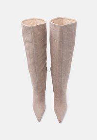 Ζευγάρι ψηλών μπεζ σουέντ μπότες με υφή μοτίβου κροκοδείλου, μυτερές μύτες και πλαϊνούς φερμουάρ, σε όρθια θέση σε λευκό φόντο.