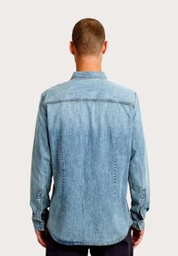 Jasnoniebieska koszula dżinsowa z długimi rękawami, zapinanymi na guziki mankietami i klasycznym kołnierzem. Posiada tylne karczki i prostą linię dołu.