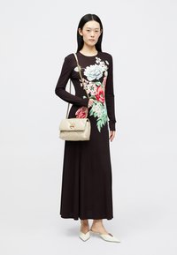 Dunkelbraunes, langärmliges Kleid mit floralem Muster in Pink und Blau. Beigefarbene gesteppte Handtasche mit goldfarbenen Beschlägen und spitze weiße Schuhe.