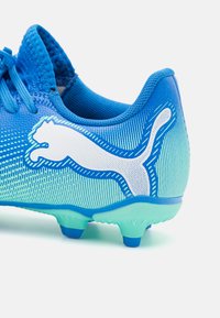 Scarpa sportiva blu con tomaia testurizzata, featuring un logo Puma bianco, design a gradiente e chiodi leggeri per la trazione.