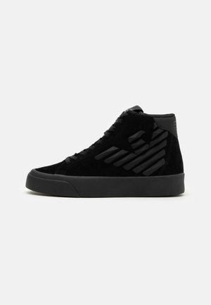 Sort høj top sneaker med tyk sål, snørelukning foran og diskret diagonal stribedesign på siden.