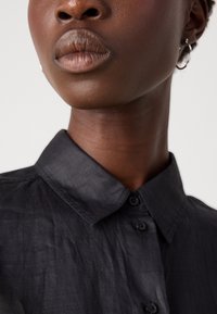 Camicia nera con colletto in tessuto testurizzato, con chiusura a bottoni, caratterizzata da una leggera lucentezza e un design del colletto strutturato.