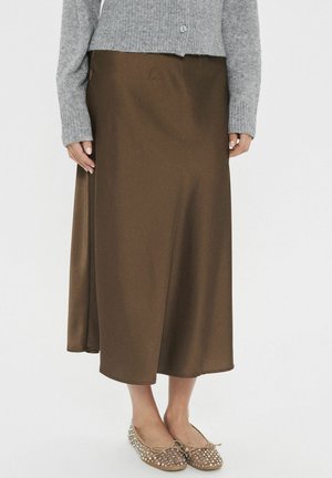 Brown satin midi skirt with a smooth texture, paired with a light gray knitted cardigan and beige flats adorned with silver studs.