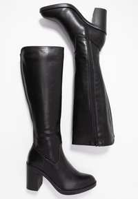 Botas de cuero de color negro hasta la rodilla, con un alto tacón bloque, cremallera lateral y textura suave con detalles de costura mínimos.