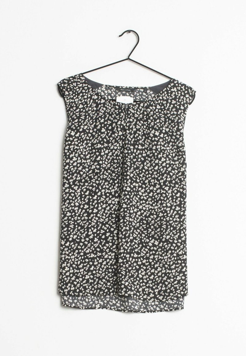 Blouse noire sans manches avec petit imprimé floral blanc suspendue sur un cintre noir sur fond blanc.