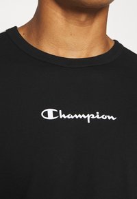 Schwarzes Baumwoll-T-Shirt mit Rundhalsausschnitt und einem weißen "Champion"-Logo auf der Brust, das eine glatte Textur und ein lässiges Design präsentiert.