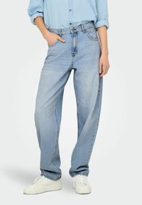 Svijetloplave visokotarzne traperice opuštenog kroja, s pet džepova, petljama za remen i izblijedjelom denim teksturom. Uparene s bijelim tenisicama.