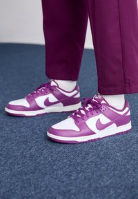 Sapatilhas Nike roxas e brancas com um cabedal de couro suave, caixa do dedo perfurada e atacadores planos. Sola de borracha com ranhuras para aderência.