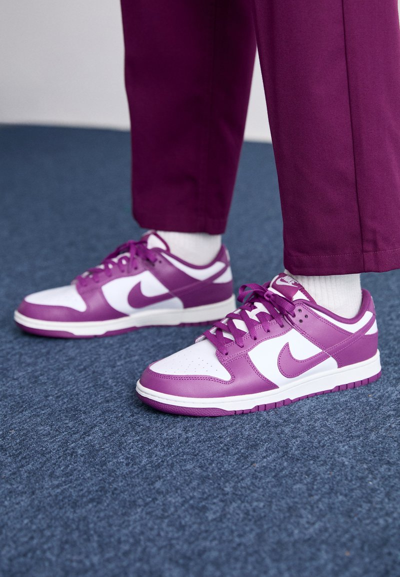 Zapatillas Nike en púrpura y blanco con parte superior de cuero suave, caja de puntera perforada y agujetas planas. Suela de goma con textura para mayor agarre.