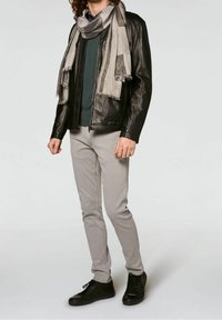 Giacca di pelle nera sopra una camicia verde scuro, sciarpa grigia, jeans grigi chiari e sneakers nere. Silhouette slim-fit con dettagli testurizzati.