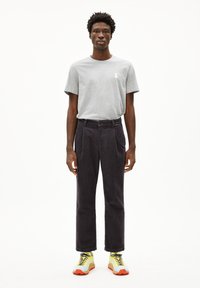 Grijze katoenen t-shirt, donkere corduroy broek met plooien, en felgele sneakers. Casual outfit met onderscheidende texturen en kleuren.