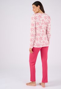 Langärmliges Oberteil mit pinkem Blumenmuster auf weißem Hintergrund, kombiniert mit gerippten rosa Hosen. Weicher Stoff, entspannte Passform, keine sichtbaren Beschläge.