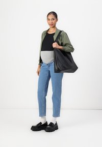 Borsa tote in pelle nera, giacca verde oliva, top nero, cintura grigia, jeans azzurri chiari e scarpe chunky nere con calze bianche.
