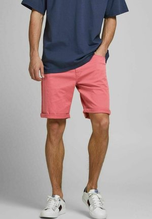 Hellrosa Baumwollshorts mit umgeschlagenen Säumen, kombiniert mit einem navyblauen T-Shirt und weißen Sneakers, im lässigen Design und mit lockerer Passform.
