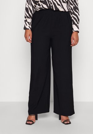Person wearing black wide-leg pants, zebra print long-sleeve top, and black open-toe high-heeled sandals standing on a plain background.